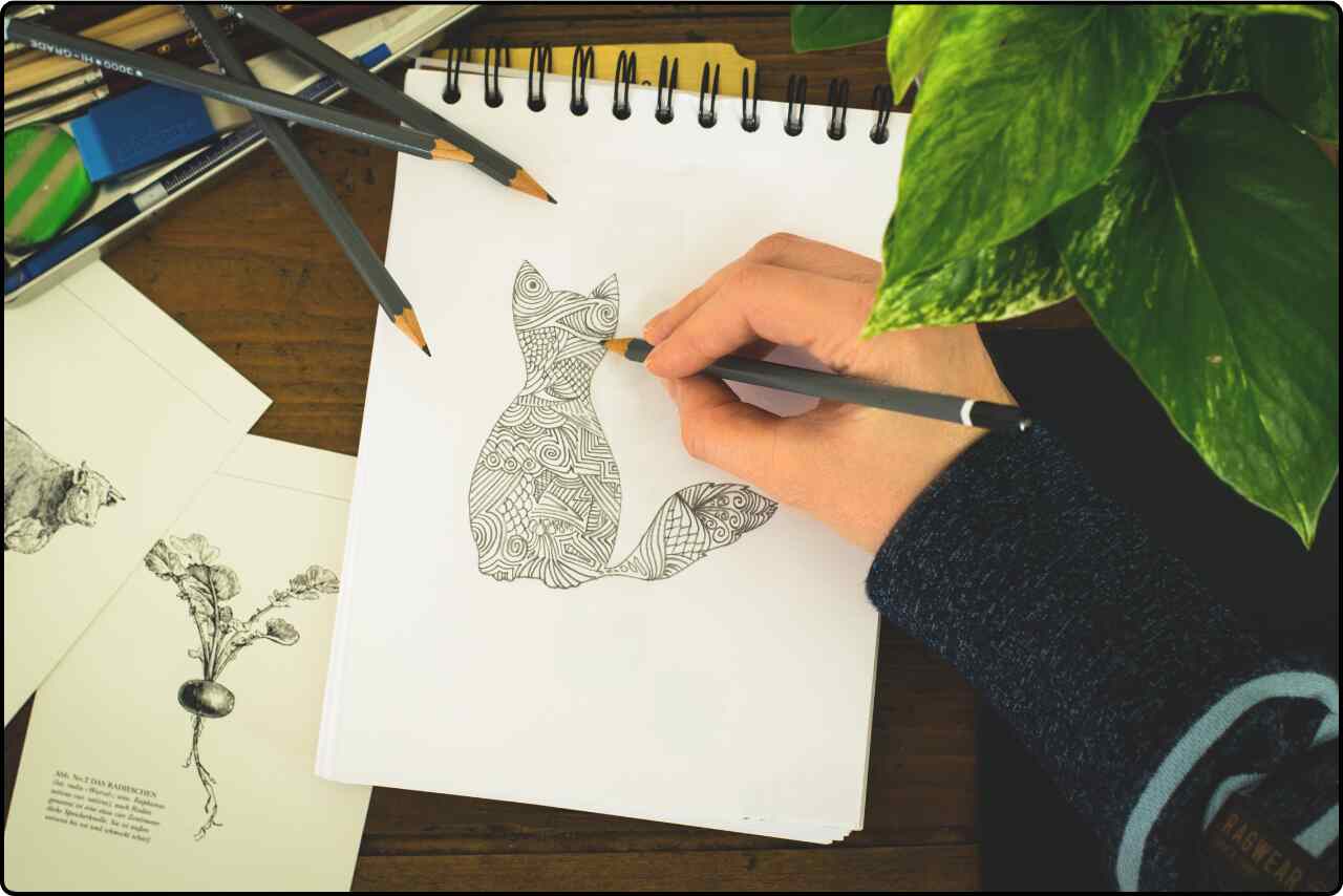 A person sketching a cat on paper with a pencil.